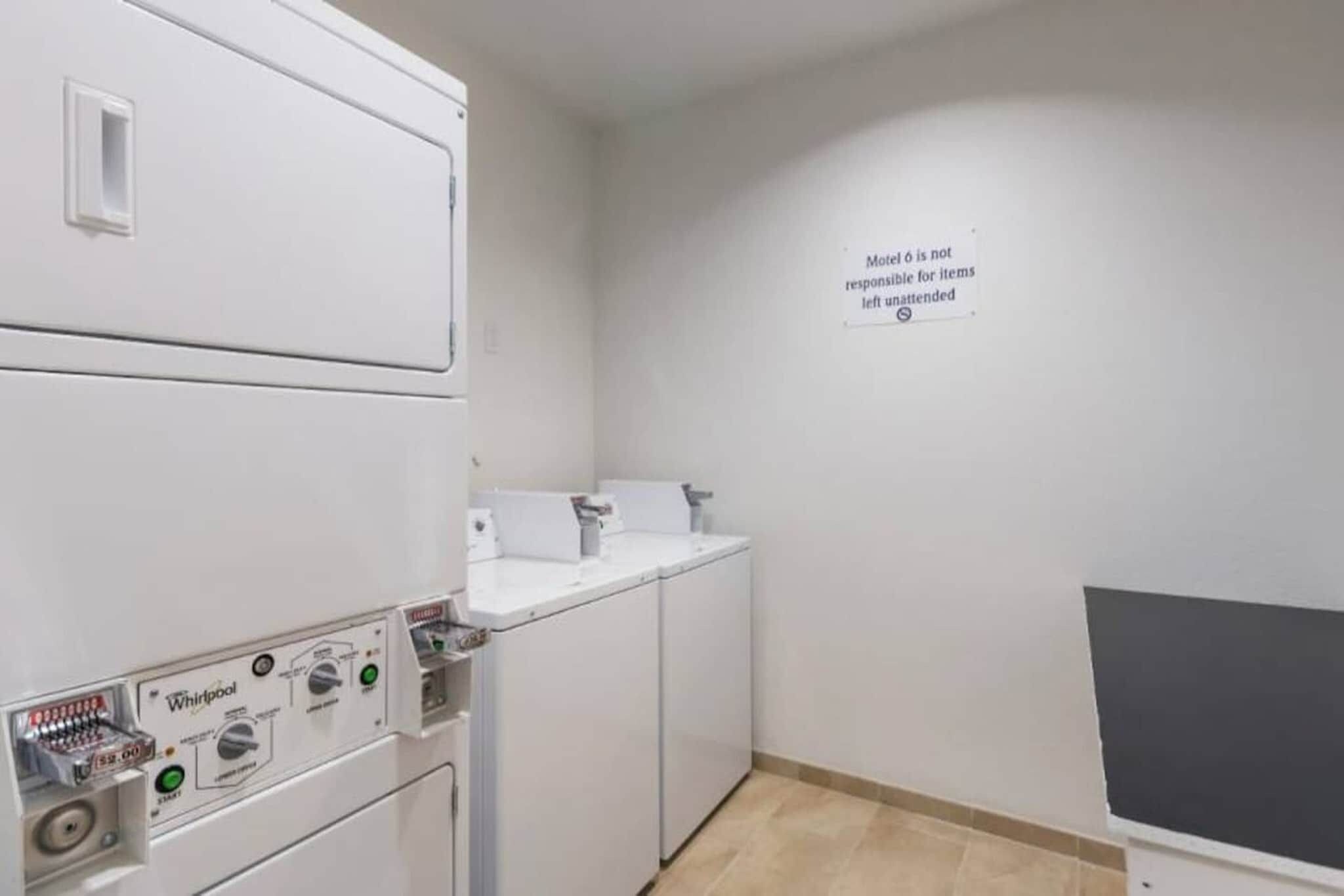 A laundry room with stacked washers and dryers, a sink, and a wall sign stating 'Motel is not responsible for items left unattended.'