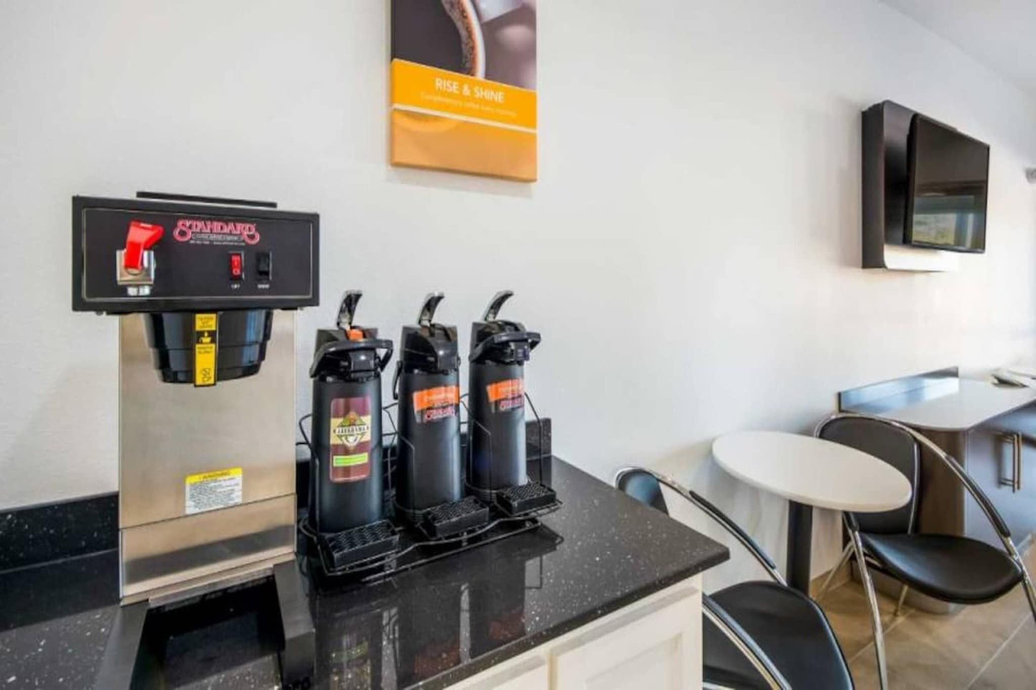 A coffee station with a coffee machine and three dispensers on a black countertop.