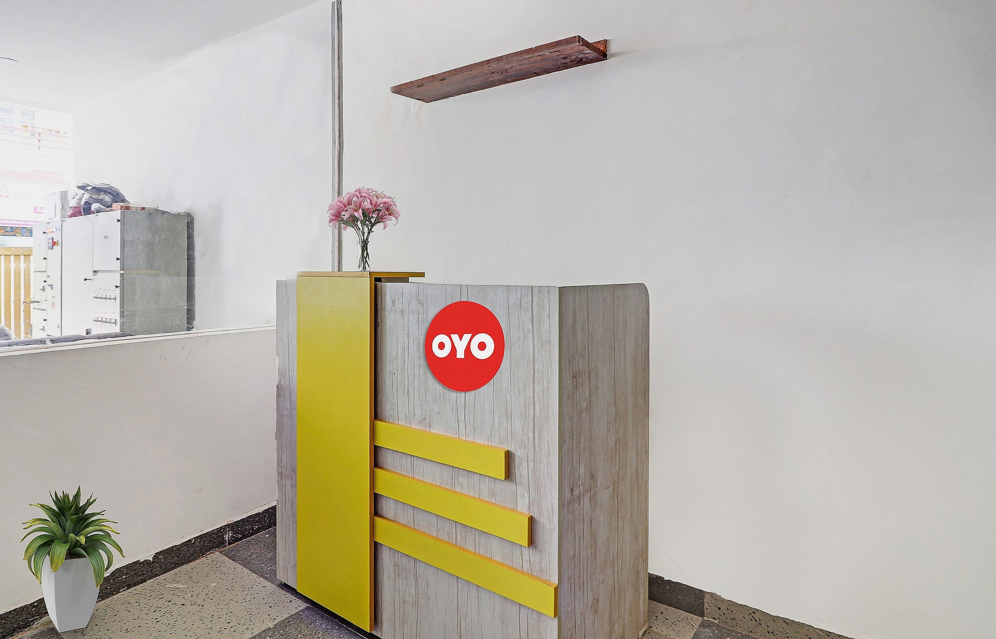 Un mostrador de recepción con un logotipo, una planta en maceta y una estantería en la pared.