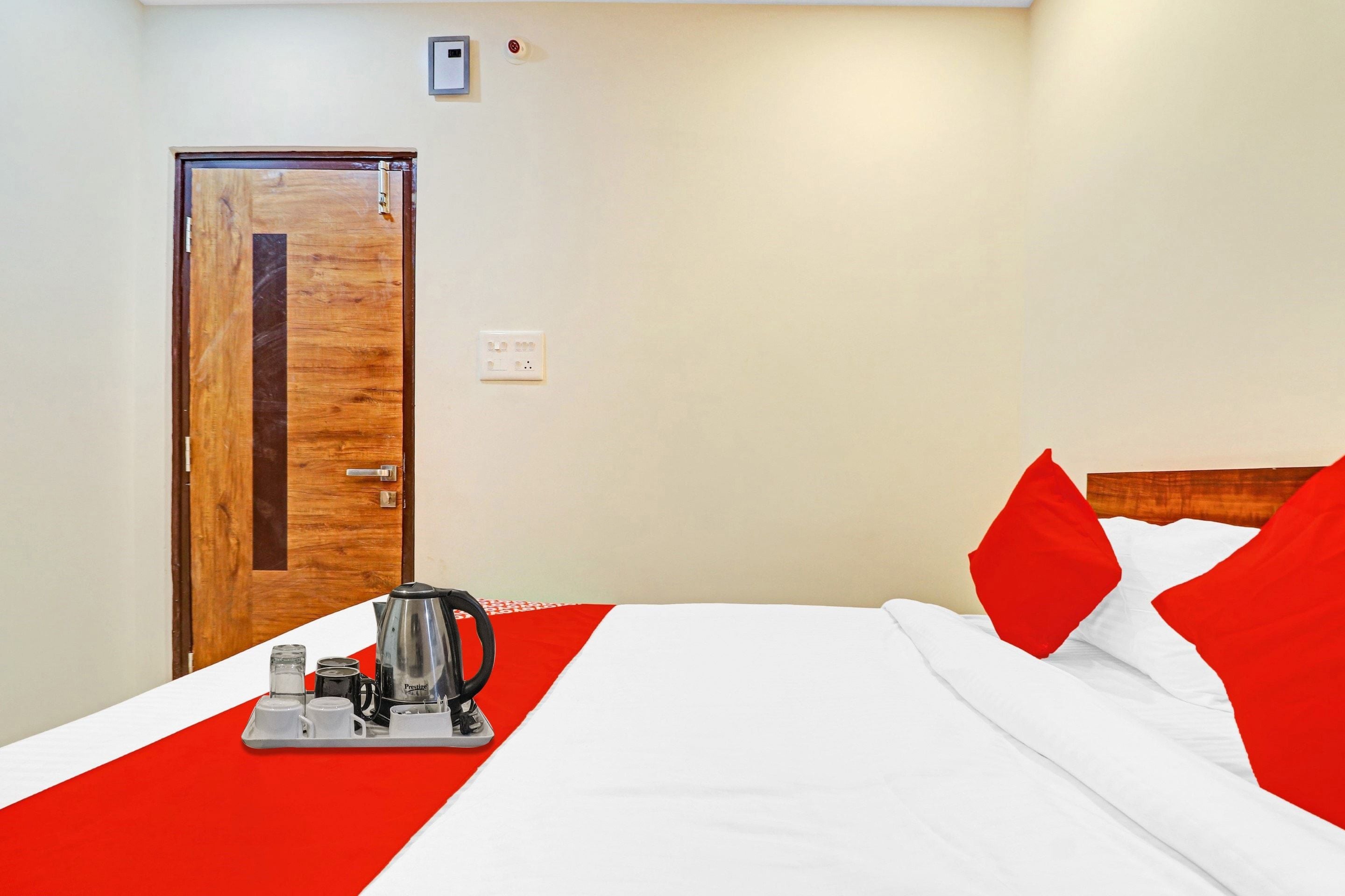 A hotel room with a wooden door, a bed with white and red bedding, and a tray with a coffee maker and cups.