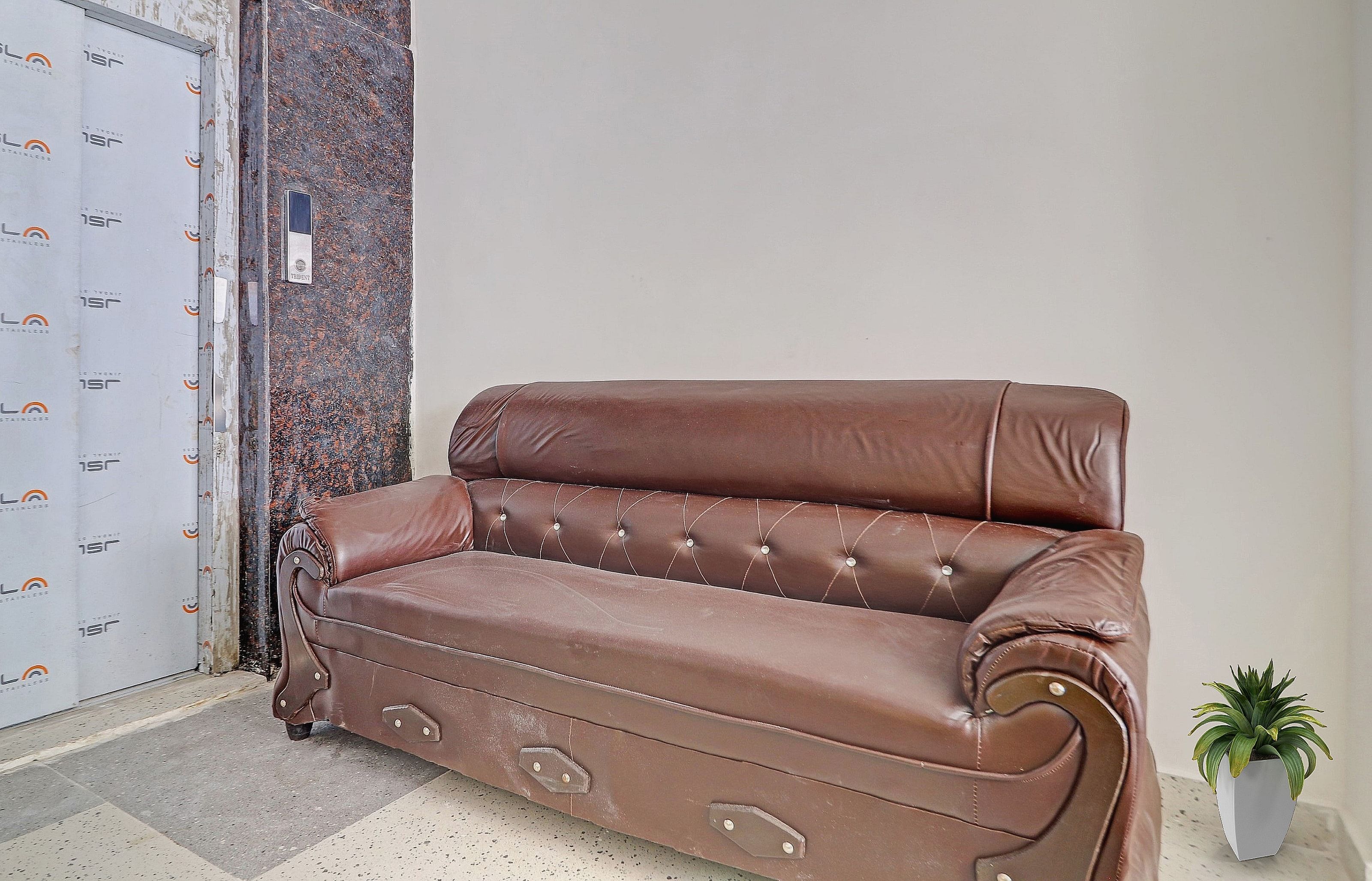 A brown leather sofa with tufted detailing and armrests, positioned against a wall with a textured pattern.