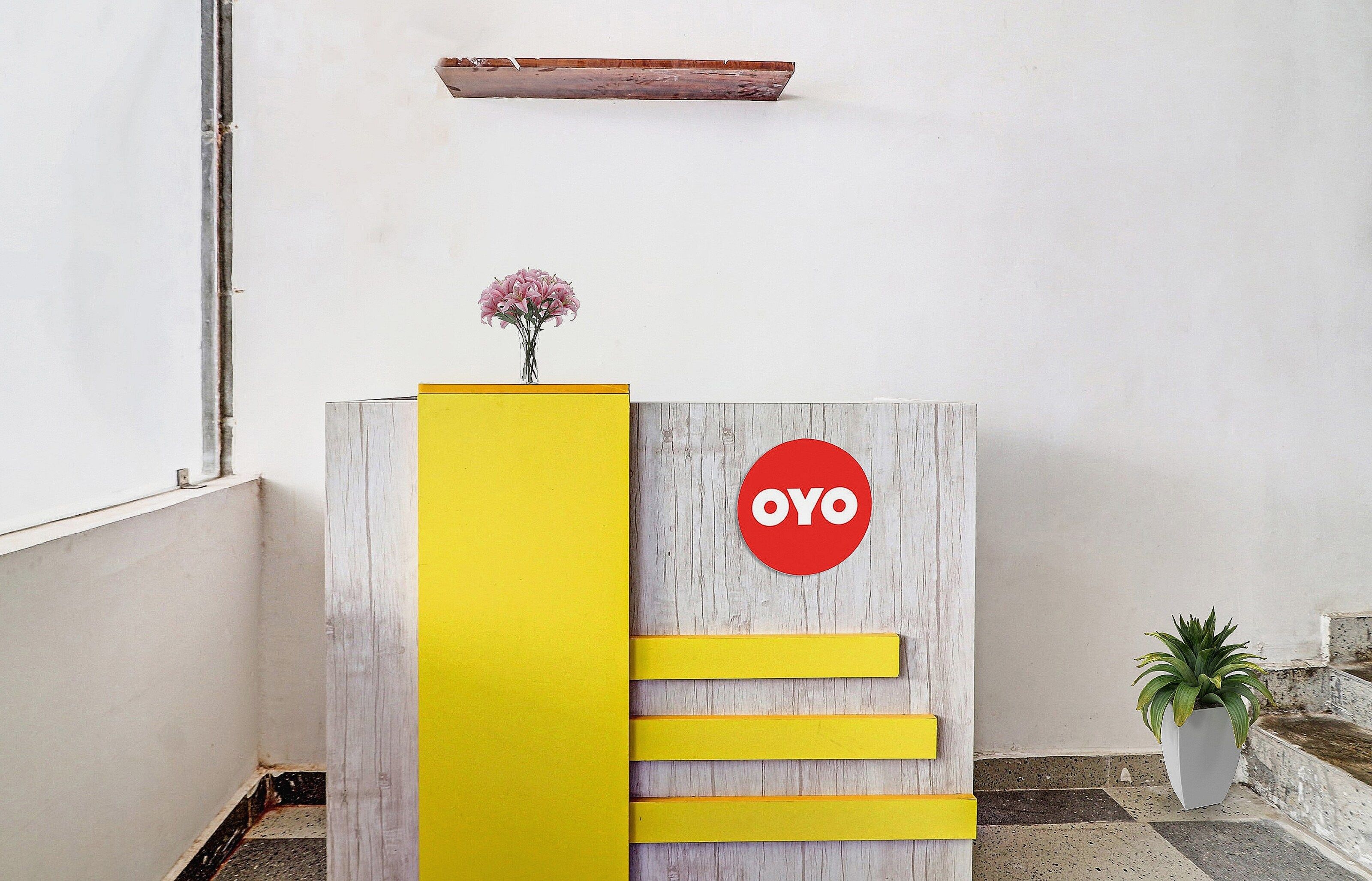 Un mostrador de recepción con detalles de madera, un panel de acento amarillo y un letrero circular rojo con la palabra 'OYO'.
