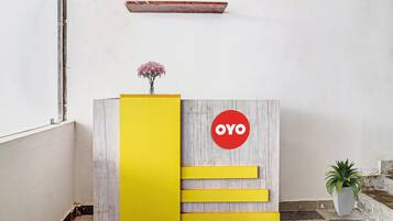 Un mostrador de recepción con detalles de madera, un panel de acento amarillo y un letrero circular rojo con la palabra 'OYO'.