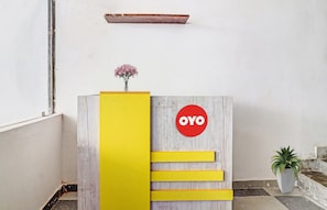 Balcão de recepção com acabamento em madeira, painel amarelo de destaque e um sinal circular vermelho com a palavra 'OYO'.