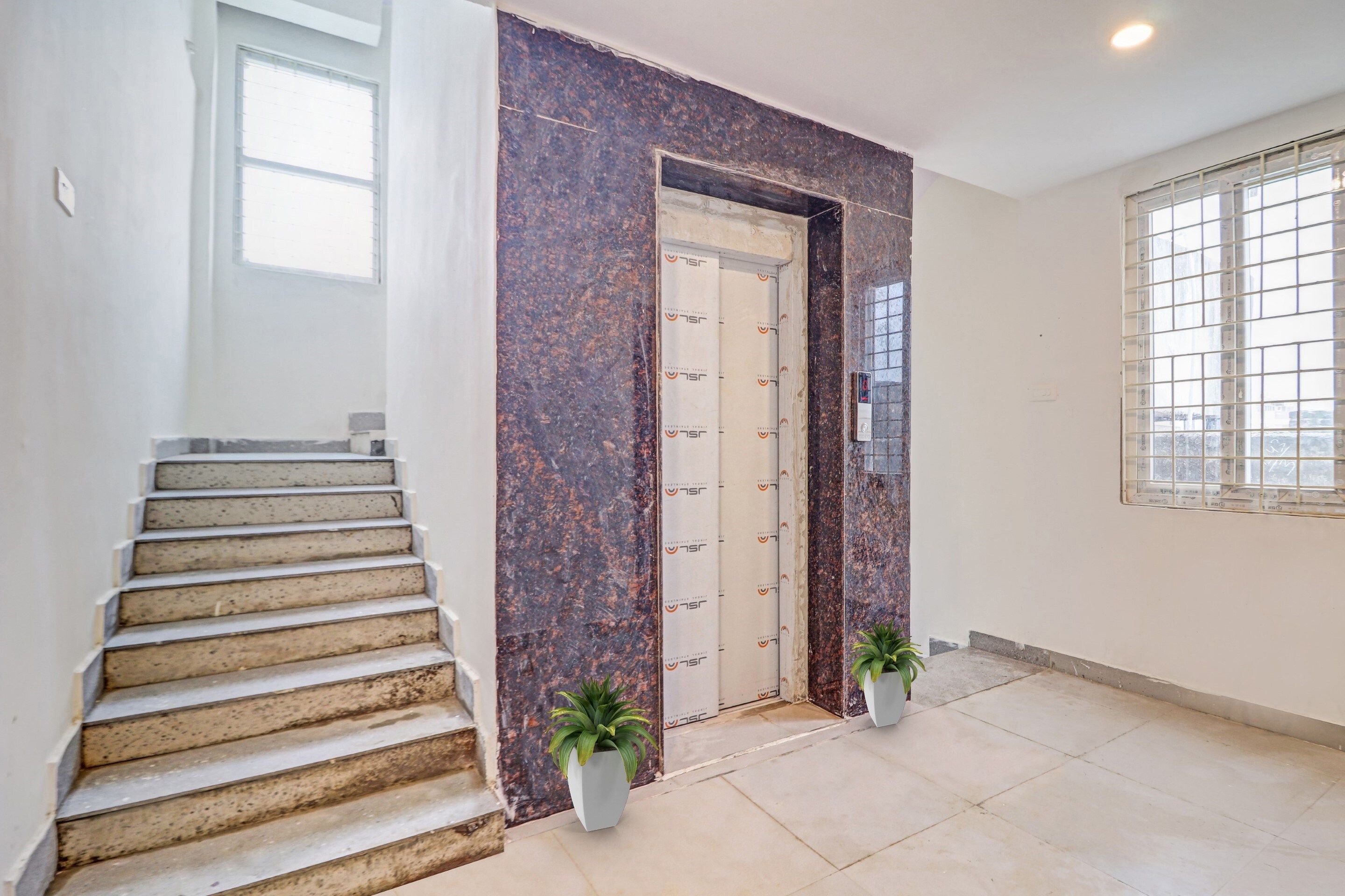 A staircase leading to a door with a textured wall, a potted plant, and a window with a grid pattern.