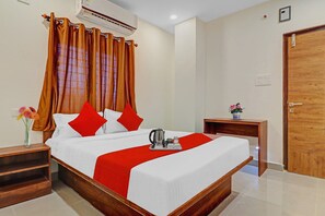 A hotel room with a bed, a nightstand, a vase with flowers, and a wooden door. - Hotel O by OYO Night Eye (Hyderabad)
