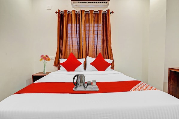 Quarto de hotel com cama, mesa de cabeceira, um vaso com flores e um tabuleiro com chaleira e xícaras.