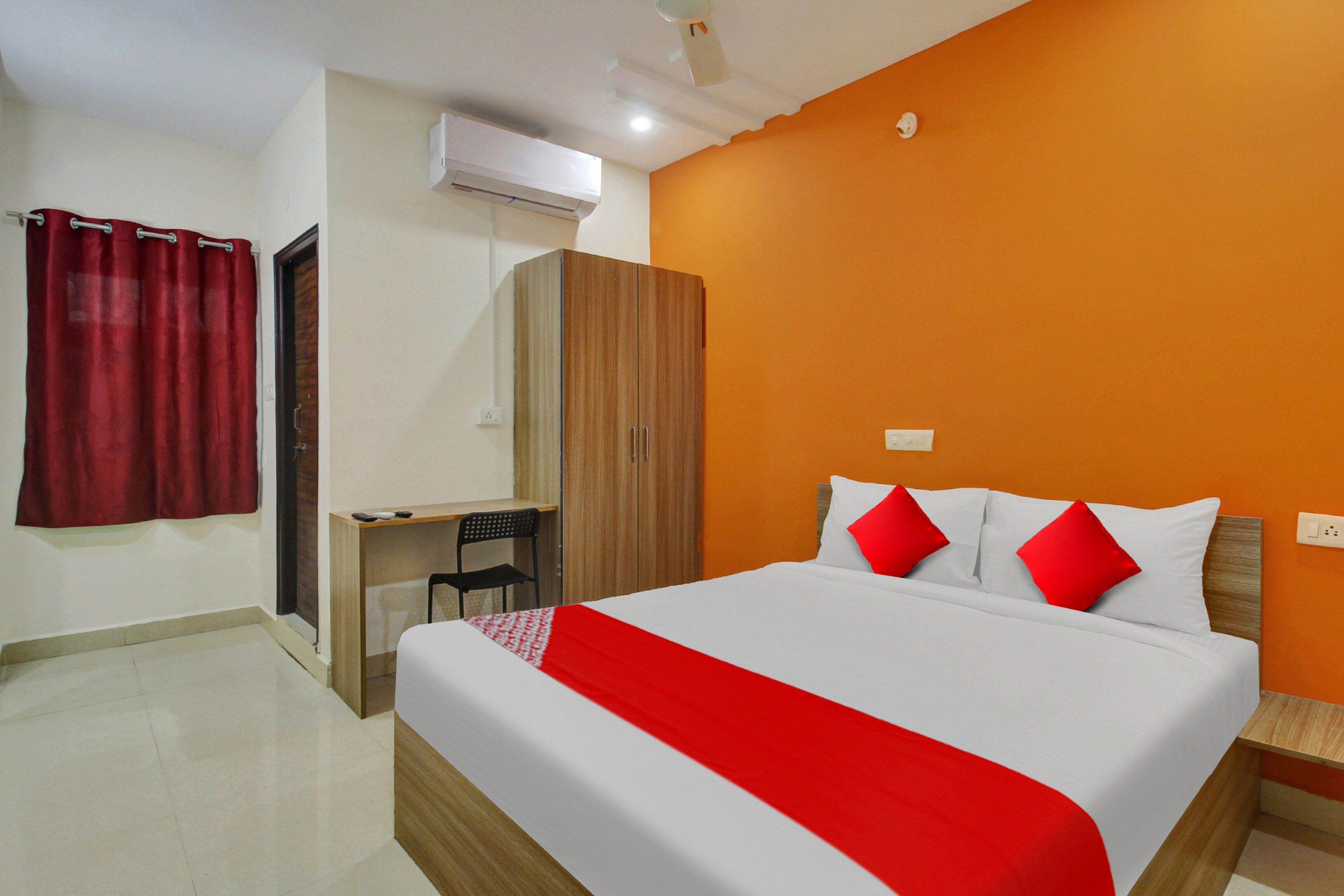 A hotel room with a bed, a desk, a wardrobe, and an air conditioning unit.