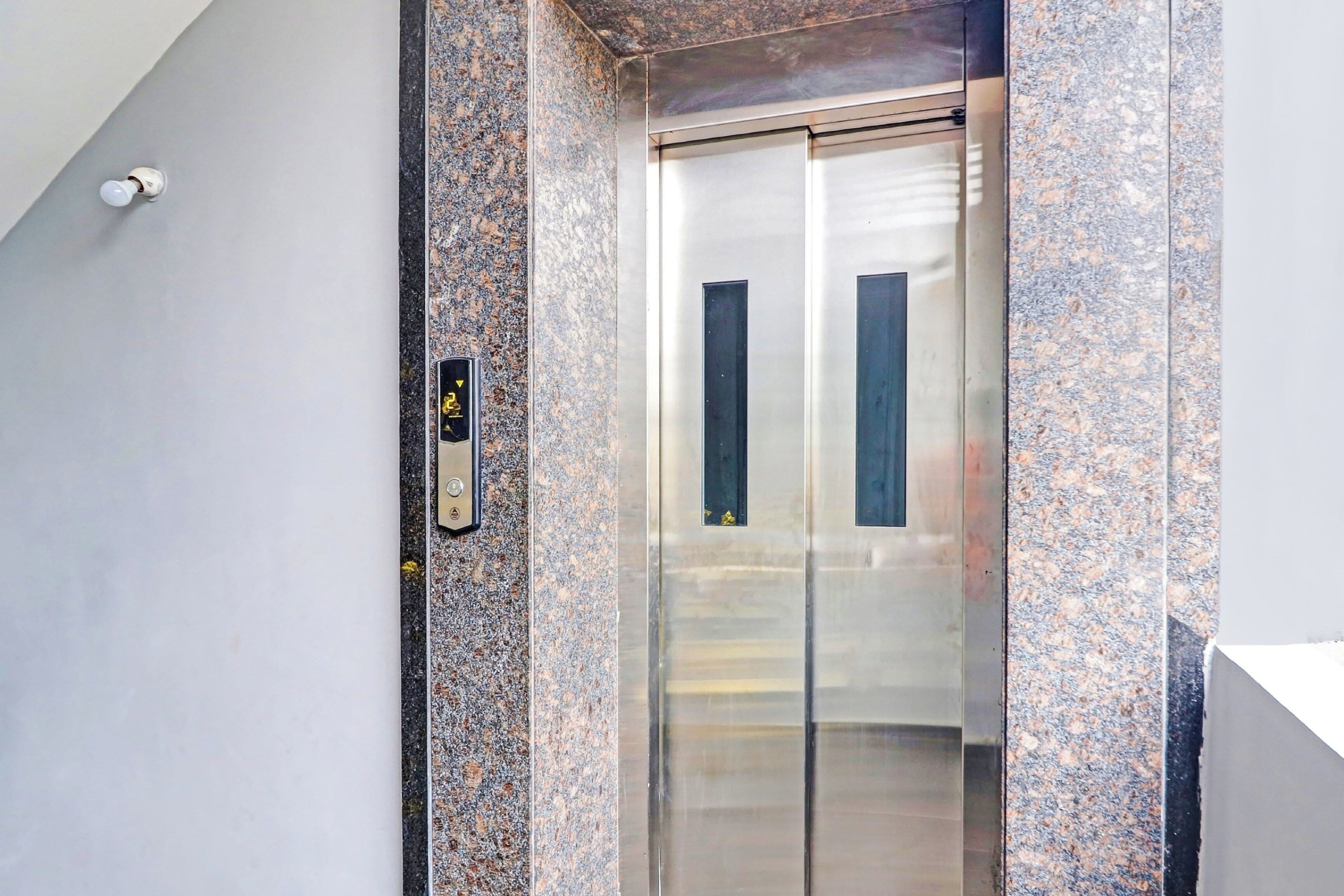 An elevator with a metallic interior and a granite wall.