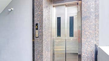 An elevator with a metallic interior and a granite wall.