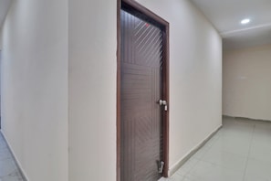 Uma porta fechada com olho de fechadura e maçaneta, um interruptor na parede e chão de azulejos.