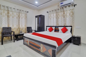 A hotel room with a bed, a desk, a chair, a wardrobe, and an air conditioning unit. - Hotel O Shri Ganesh Residency (Hyderabad)