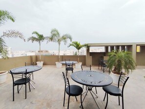 An outdoor patio area with round tables and chairs, surrounded by potted plants. - Super Collection O Rio Kondapur Near (Hyderabad)