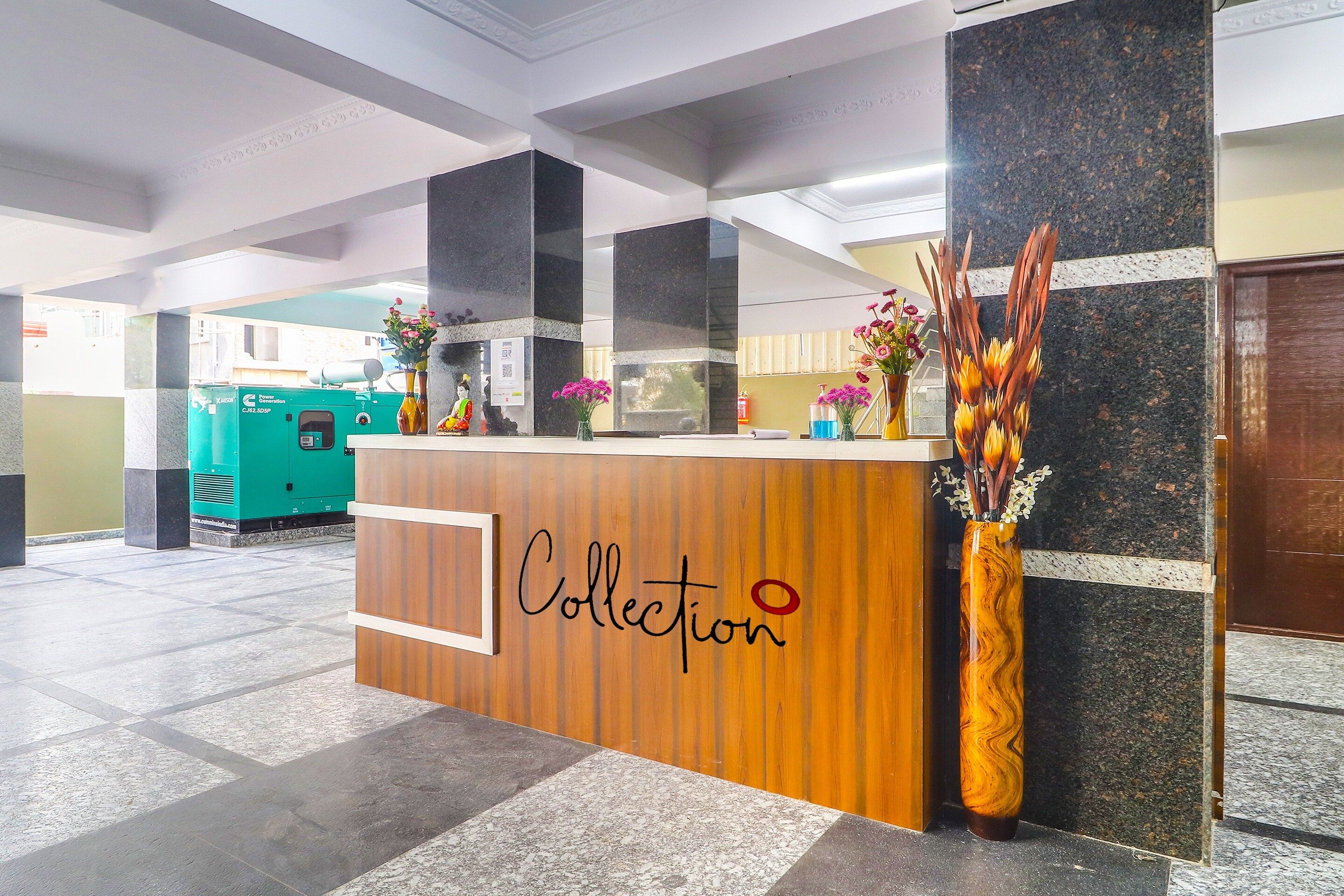 A reception desk with a wooden finish and the word 'Collection' on it, flanked by two columns and a vase with flowers.