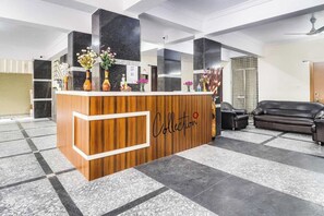 A reception desk with a wooden finish and a logo, flanked by black marble pillars, in a lobby with a checkered floor pattern. - Super Collection O Rio Kondapur Near (Hyderabad)