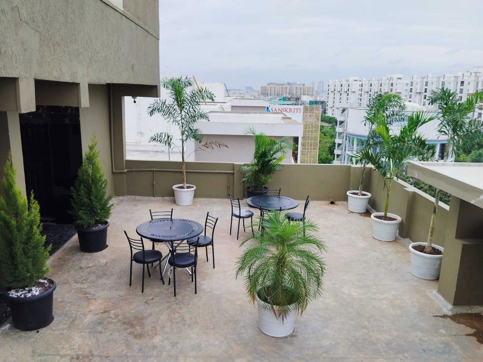 A rooftop terrace with outdoor seating, potted plants, and a view of the cityscape.