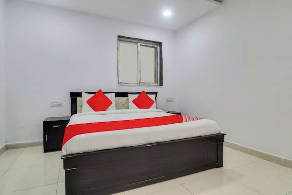 Un dormitorio con cama, mesita de noche, espejo en la pared y ventana.