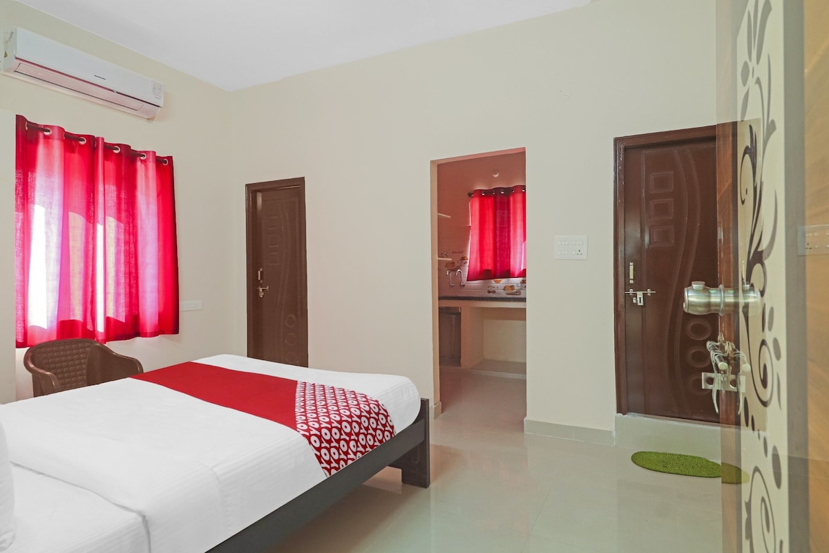 A hotel room with a bed, a chair, a desk, and a bathroom visible through an open door.