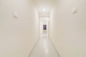 Un pasillo estrecho, bien iluminado, con paredes blancas y suelo de baldosas, que conduce a una habitación con una puerta y una cortina.