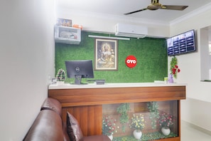 Bancada de recepção com computador, estátua de Buda emoldurada e televisão fixada na parede.