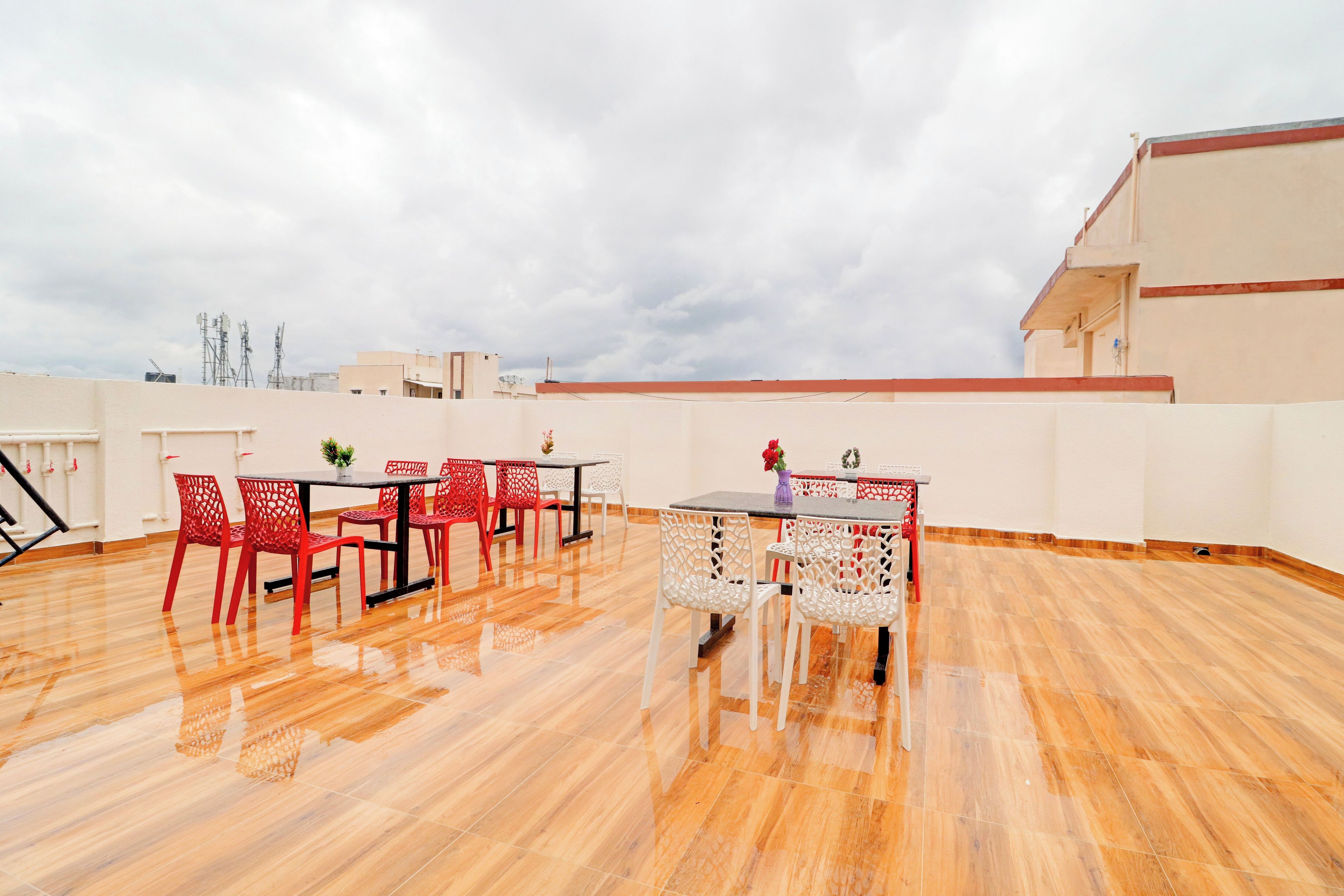 A rooftop terrace with a wooden floor, red and white chairs, and a table with a vase of flowers.