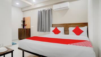 A hotel room with a bed, a wooden headboard, a red and white bedspread, a small table with a plate, and a wall-mounted air conditioner.