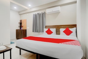 Quarto de hotel com uma cama, cabeceira de madeira, colcha vermelha e branca, uma pequena mesa com um prato e um ar-condicionado fixado na parede.