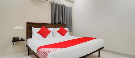 Quarto de hotel com cama, mesa de cabeceira com telefone, aparelho de ar condicionado e janela com cortinas.