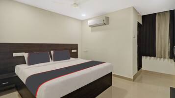 Una habitación de hotel con una cama, un ventilador de techo, un equipo de aire acondicionado y una ventana con cortinas.