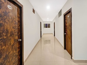 A hallway with wooden doors, a tiled floor, and a ceiling light. - Super Collection O Pnr International (Hyderabad)
