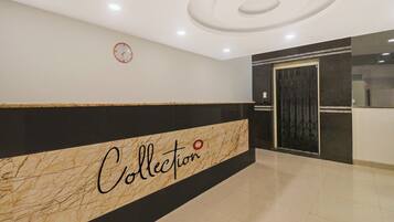 Un vestíbulo con un mostrador de recepción de mármol identificado como 'Collection' y un reloj en la pared.