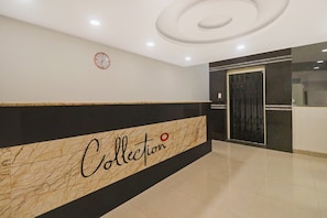 Eine Lobby mit einem Marmor-Empfangstresen mit der Aufschrift 'Collection' und einer Wanduhr.