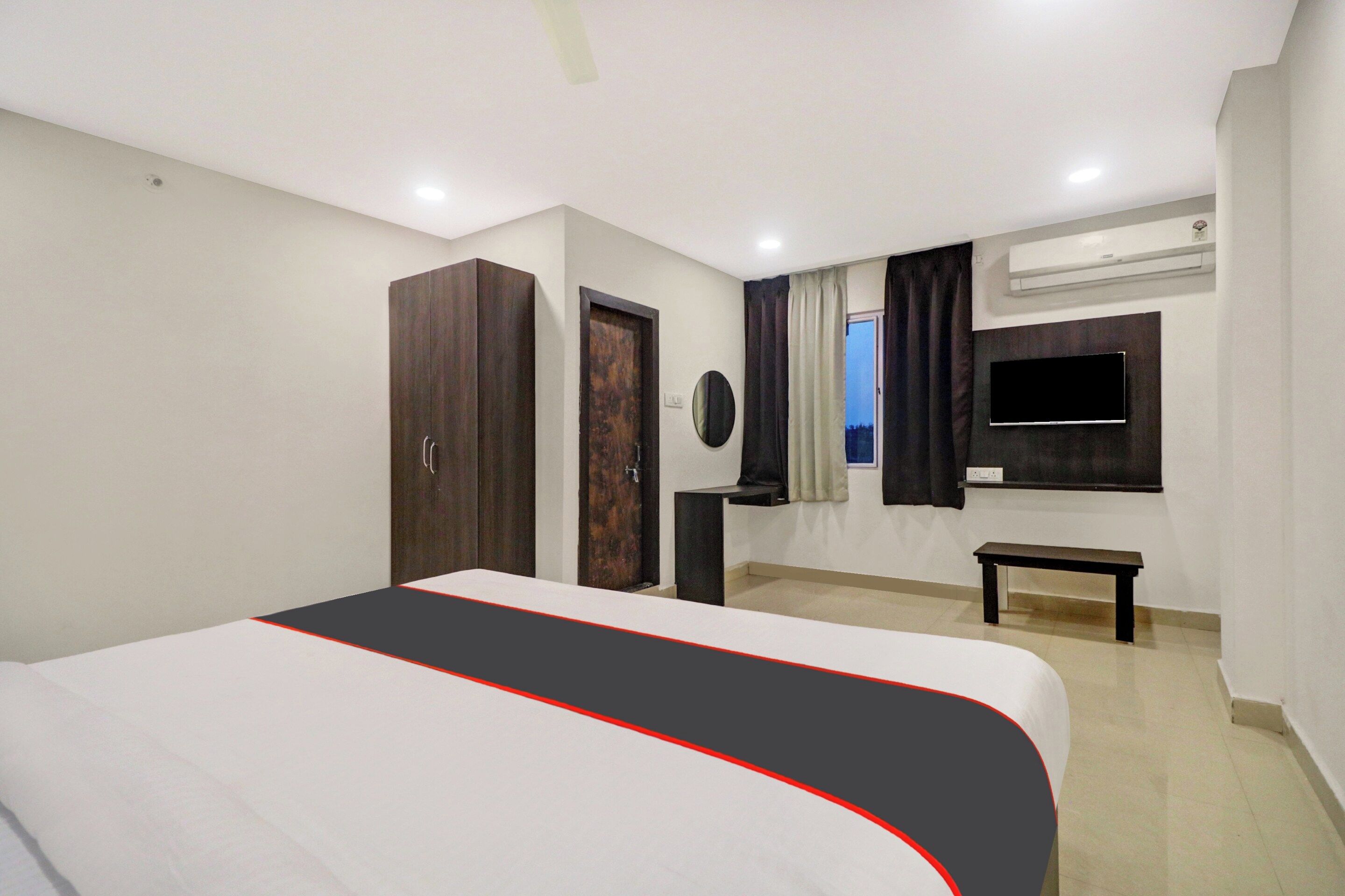 Habitación de hotel con cama, armario, mesita de noche, televisor y aire acondicionado.