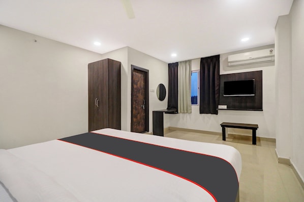 A hotel room with a bed, wardrobe, bedside table, TV, and an air conditioning unit.