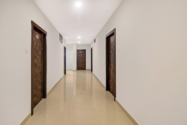 A corridor with doors on both sides, a tiled floor, and a ceiling with recessed lighting.