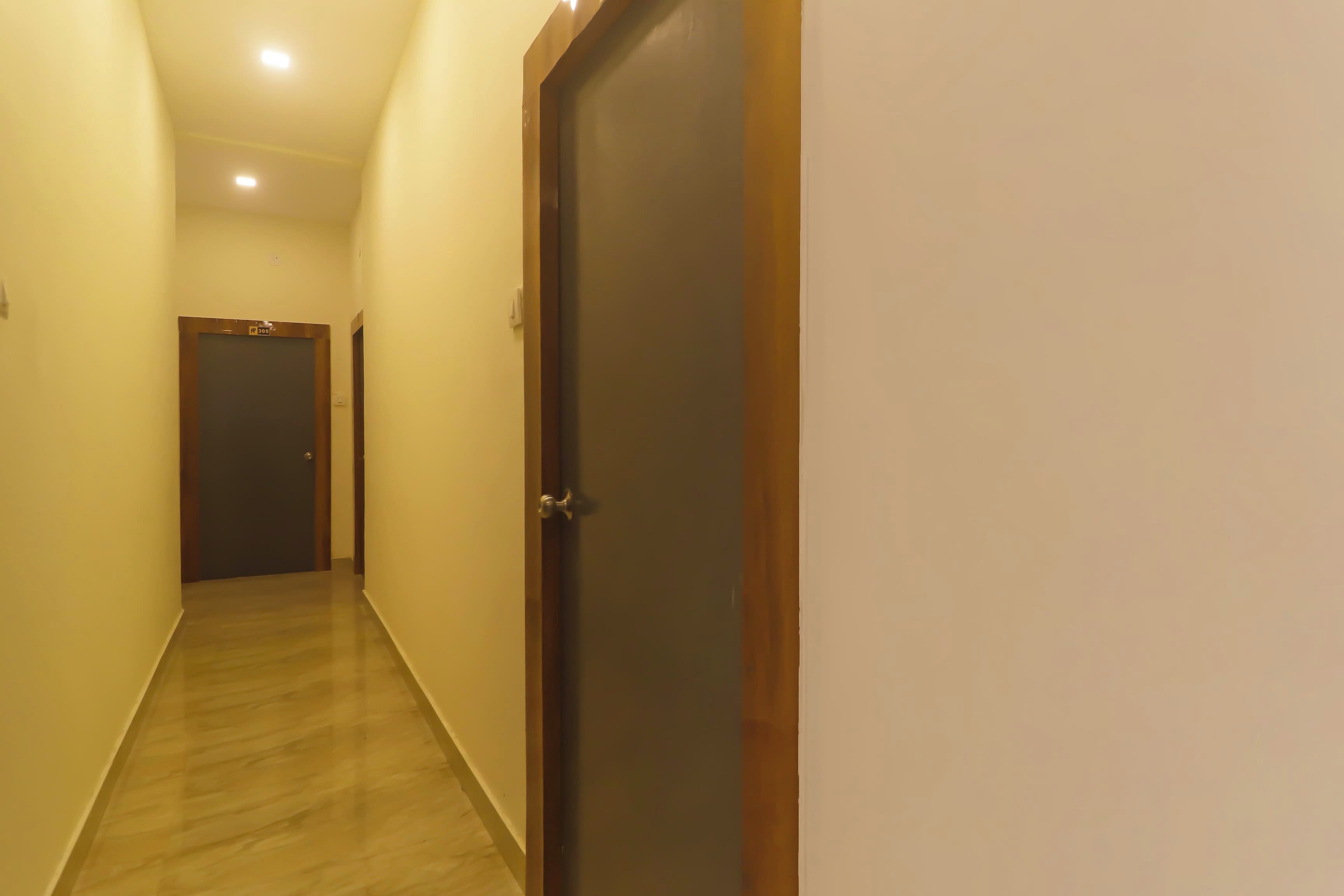 A corridor with a wooden door on the right, a door with a sign above it on the left, and a light fixture on the ceiling.