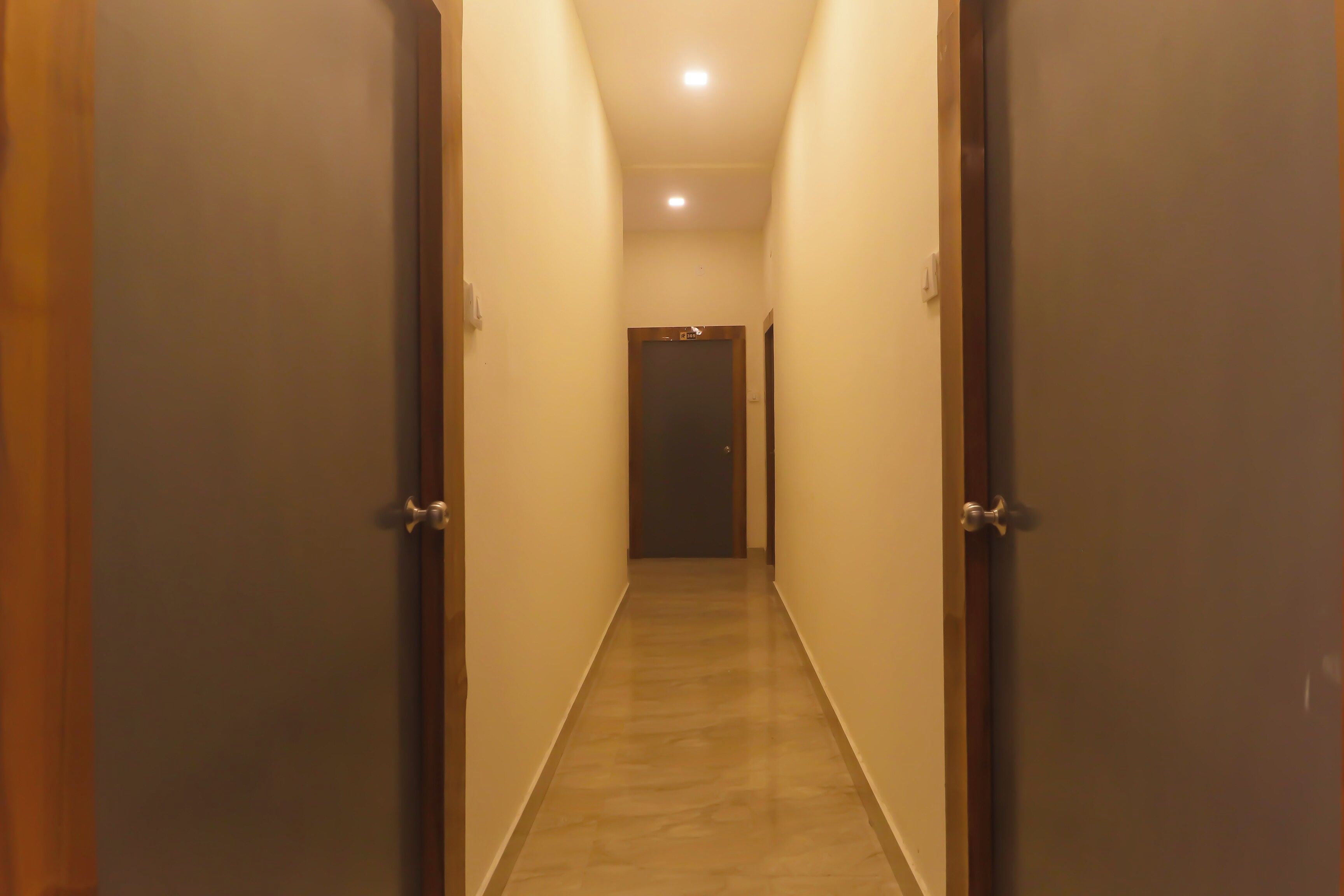 A narrow hallway with wooden doors on either side, leading to a dark room at the end.