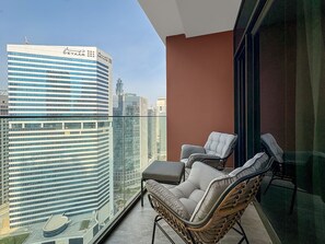 A balcony with wicker chairs, a small table, and a view of high-rise buildings. - Modern Studio with Canal Views in Peninsula Two (Dubai)