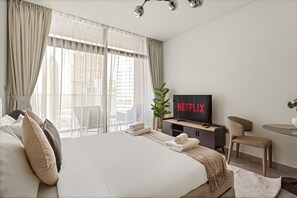A modern hotel room with a large bed, a television displaying the Netflix logo, a small desk, a chair, and a plant. - Modern Studio with Canal Views in Peninsula Two (Dubai)