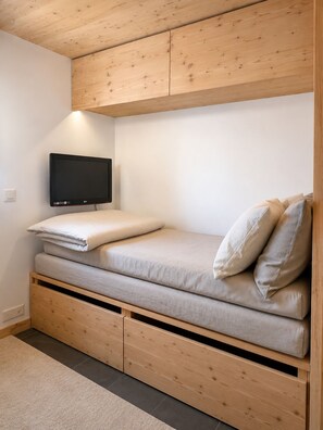 A compact room with a bed, a television mounted on the wall, and a wooden ceiling. - New Listing (Verbier)