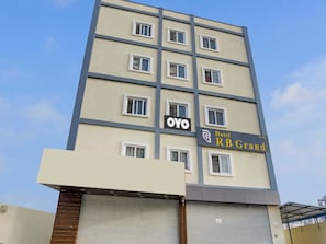 Un edificio de hotel de varios pisos con un letrero que dice 'Hotel RB Grand' y el logotipo de 'OYO'.