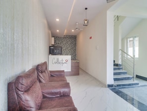 Un área de recepción con mostrador, un sofá de cuero marrón, un muro con diseño, un ventilador de techo y una escalera.