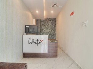 Un mostrador de recepción con el rótulo 'Collection', una televisión y un papel tapiz decorativo en la pared de fondo.