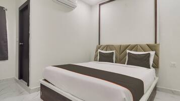Una habitación de hotel con cama, puerta, equipo de aire acondicionado y espejo montado en la pared.