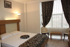 A hotel room with a bed, a chair, a desk, a lamp, and a window with curtains. - Real Residence Otel (merkez)