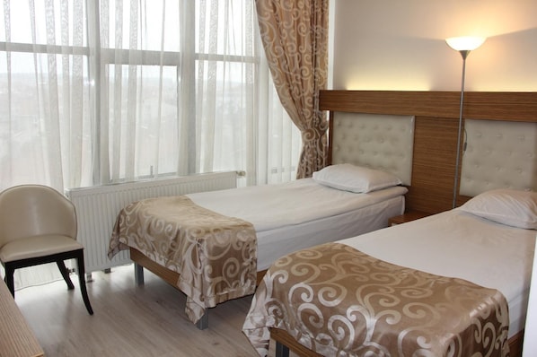 A hotel room with two beds, a chair, a radiator, and a lamp.