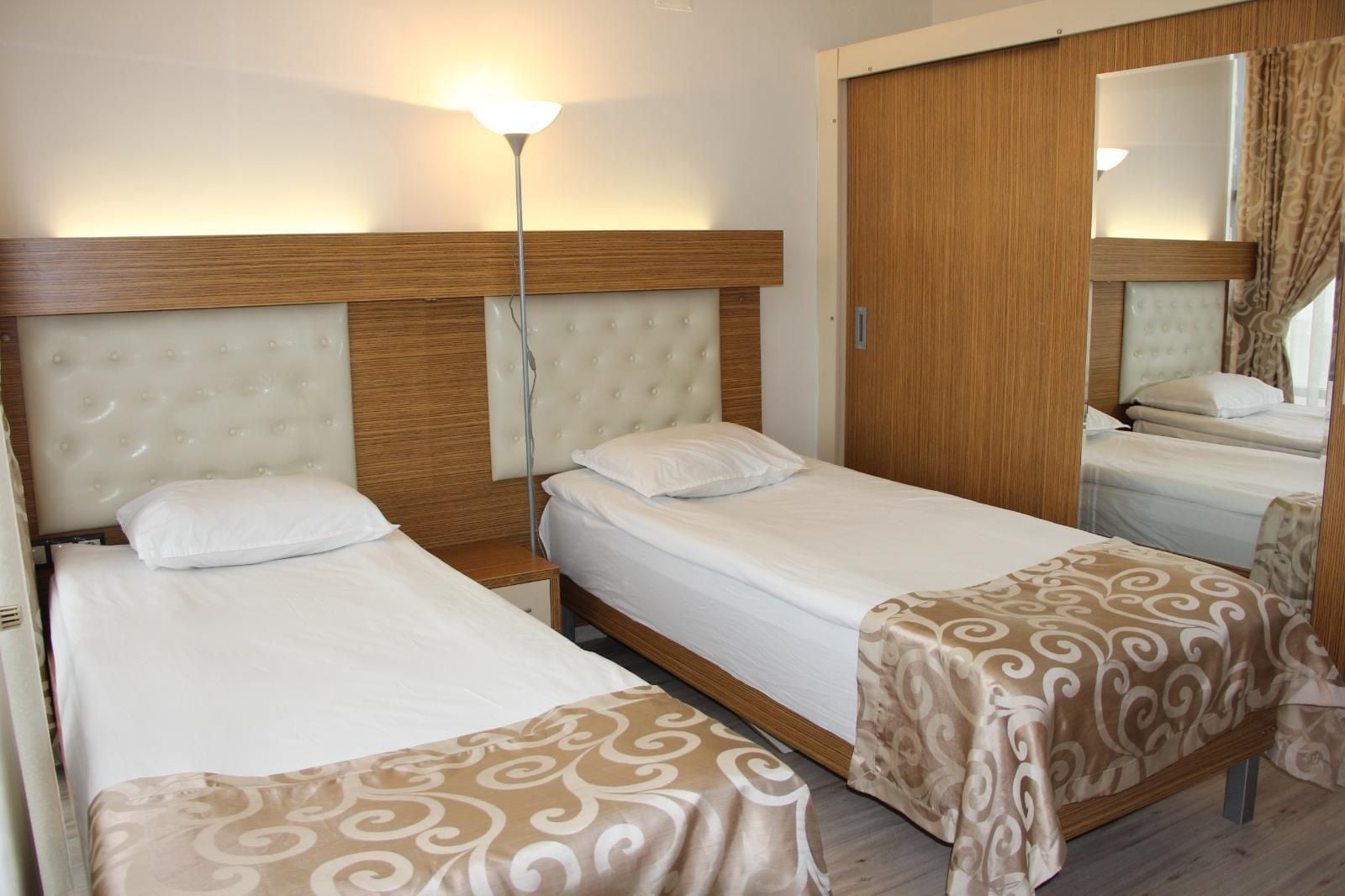 Une chambre d’hôtel avec deux lits, un grand miroir et une lampe sur pied.