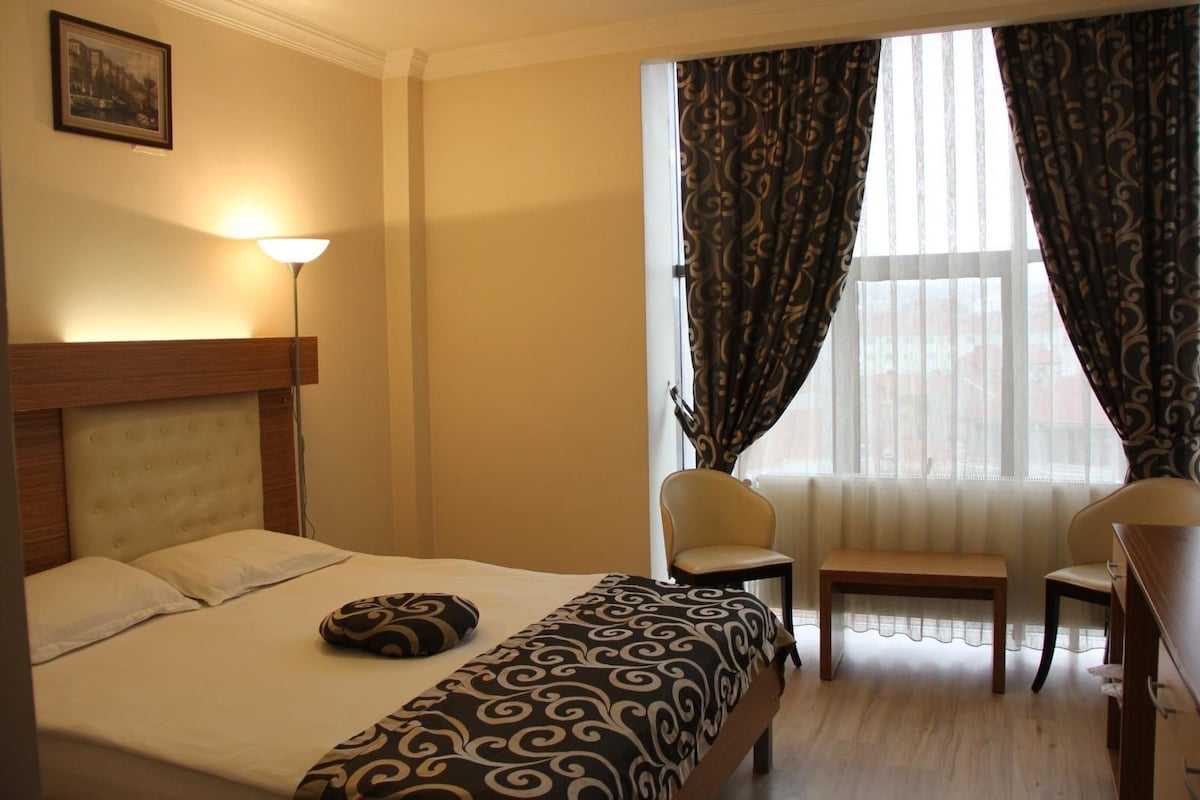 A hotel room with a bed, two chairs, a desk, a lamp, and a window with curtains.