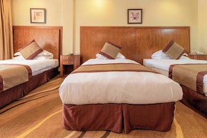 Ein Hotelzimmer mit drei Betten, jedes mit einem hölzernen Kopfteil, weißer Bettwäsche und braunen Akzenten.