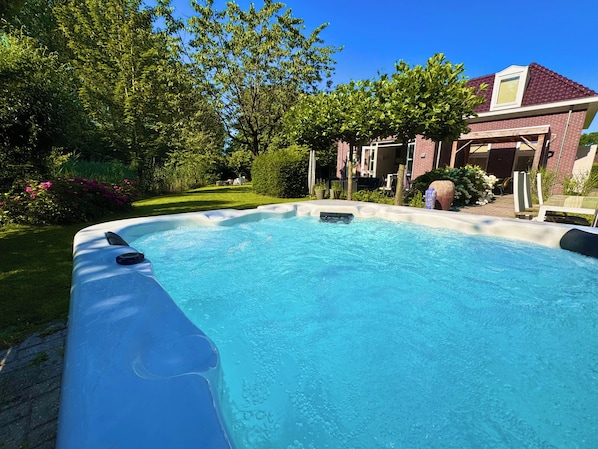 Ein Whirlpool in einem Garten mit einem Ziegelhaus und üppiger Bepflanzung.